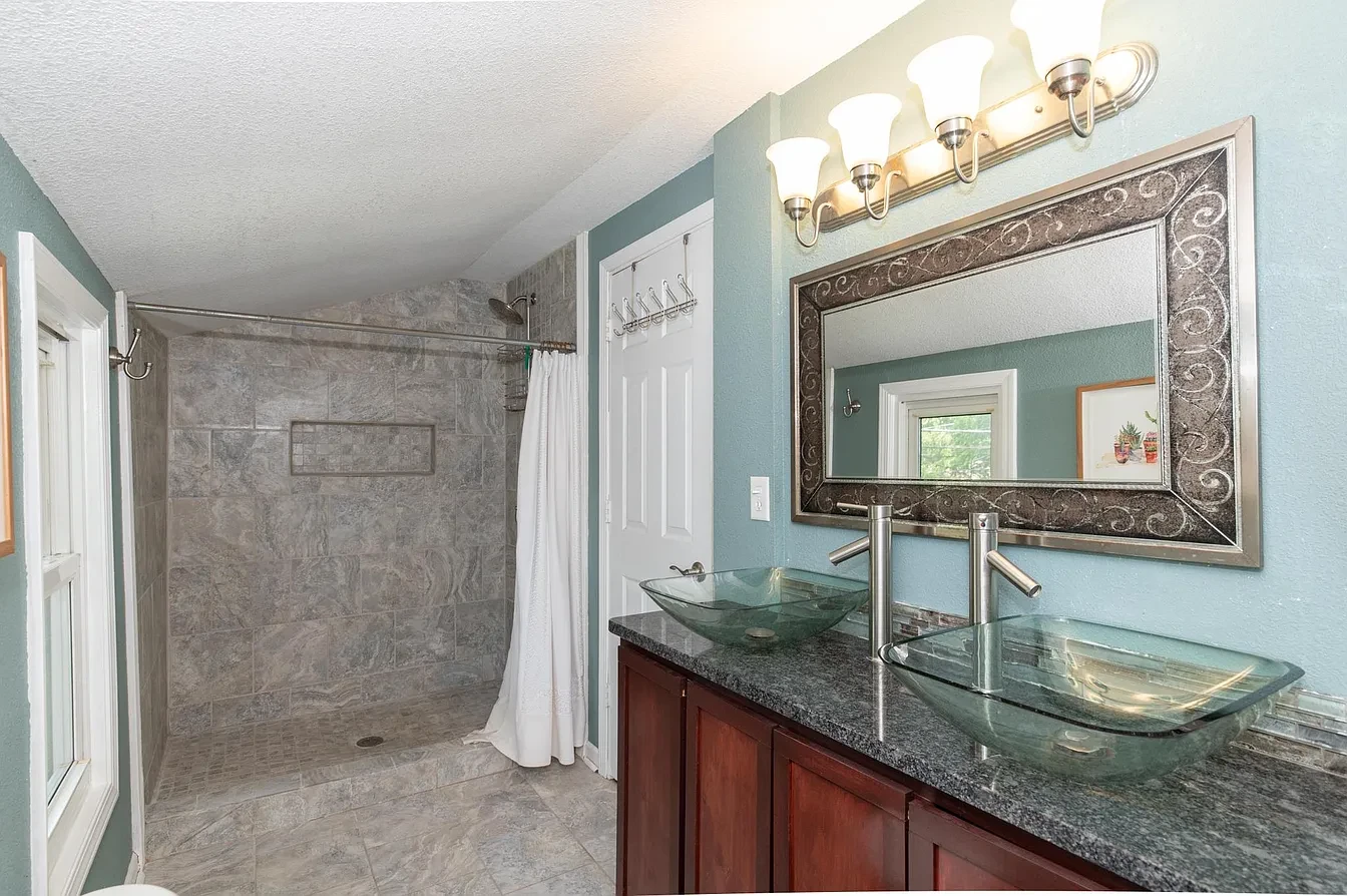 Bathroom — dual glass vessel sinks with teal walls, tile shower and ornate mirror