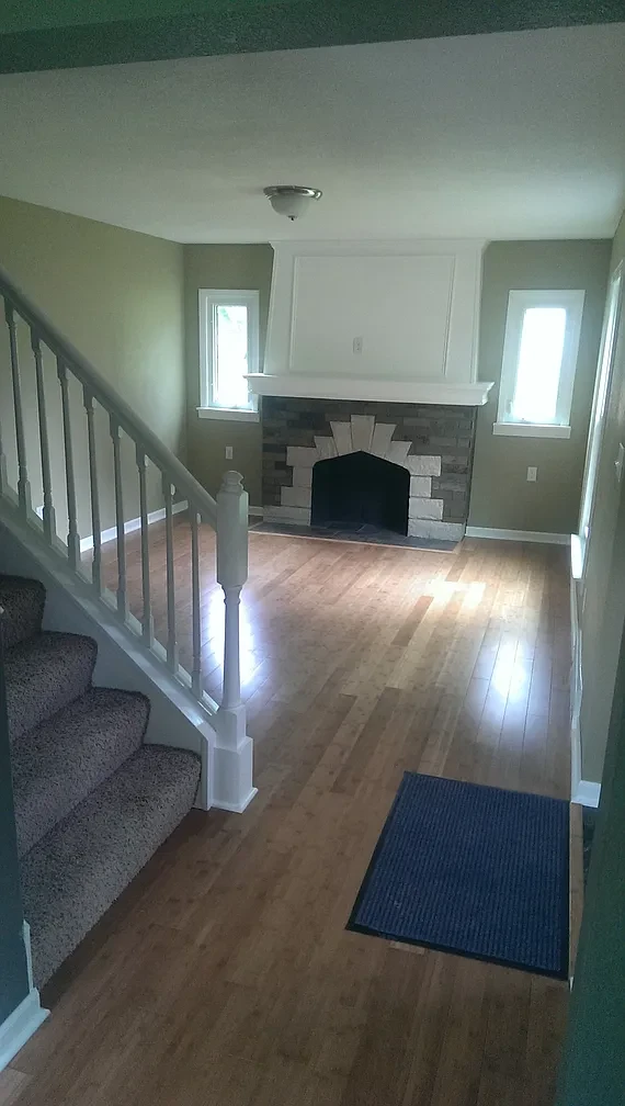 Living room — staircase entry with stone fireplace and hardwood floors